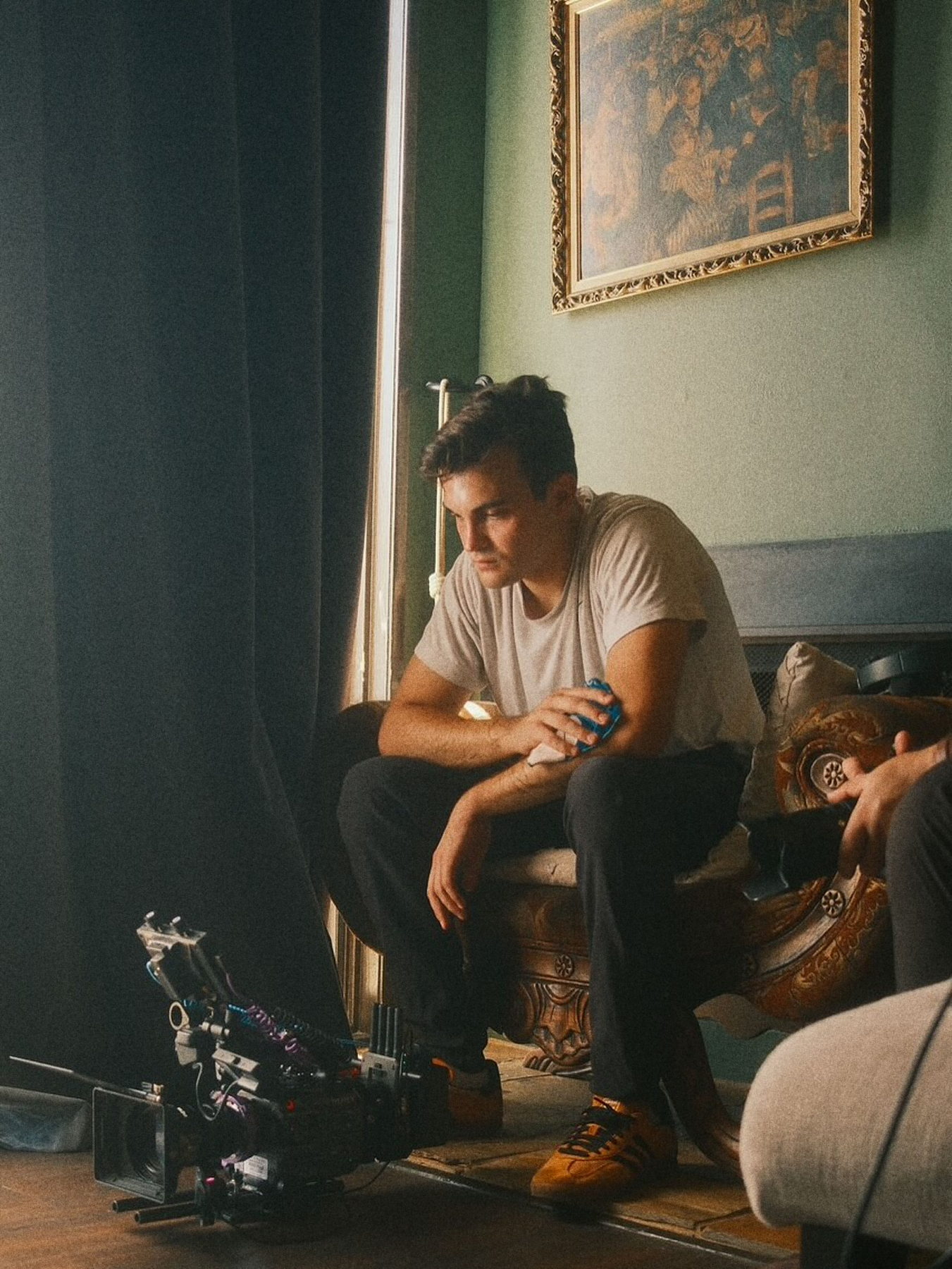 Javier Calleja seated by a window on set, looking down, a cinema camera on the floor at his feet