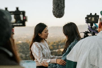 Two performers rehearsing on the hilltop with the camera crew around them