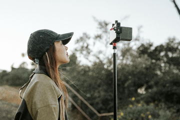 A crew member in a cap looking up beside a light stand on the hillside