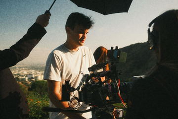 Javi at the camera under a flag on a hillside at golden hour