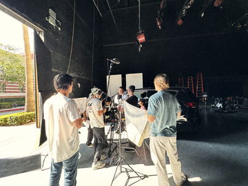 Crew holding a patterned cloth beside the camera at the stage door