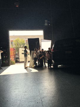 The stage door in full daylight, crew working in silhouette by the car