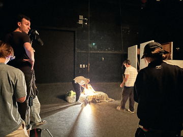 A single lamp lit inside the bedding prop, crew looking on