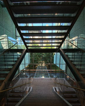 A glass footbridge seen along its length, stairs overhead