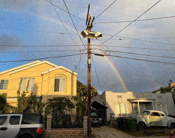 A rainbow behind a utility pole and a yellow house
