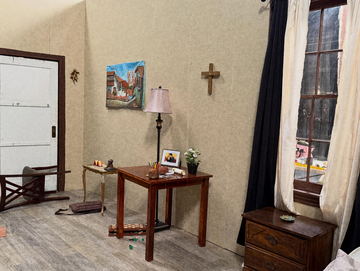 A sparse room set with a crucifix, a lamp and a small painting