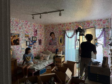 A bedroom set with floral wallpaper while a crew member adjusts a light
