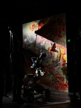 A graffiti wall flat lit on a dark stage with the camera in silhouette